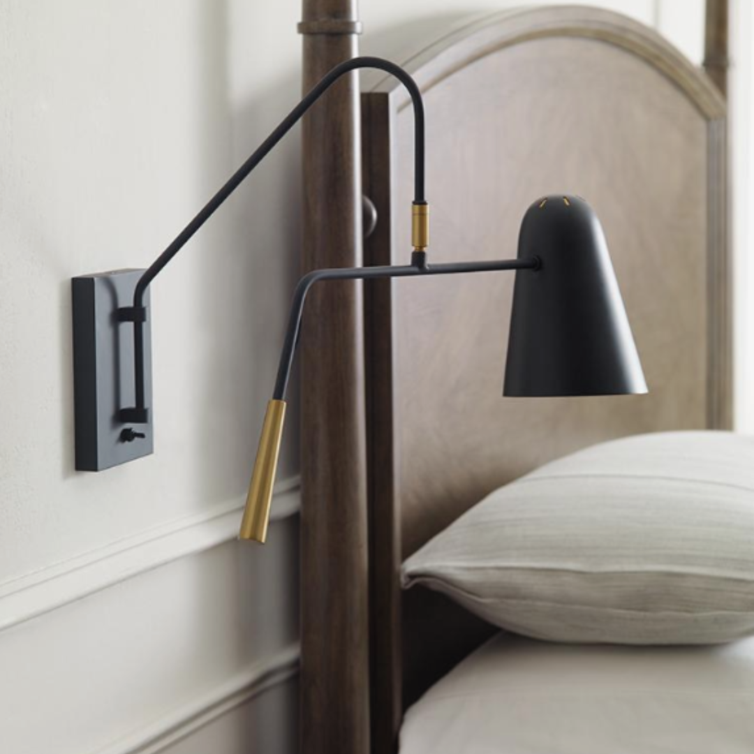 Mid Century style black wall-mounted lamp with brass accents beside a curved wooden headboard and neutral bedding