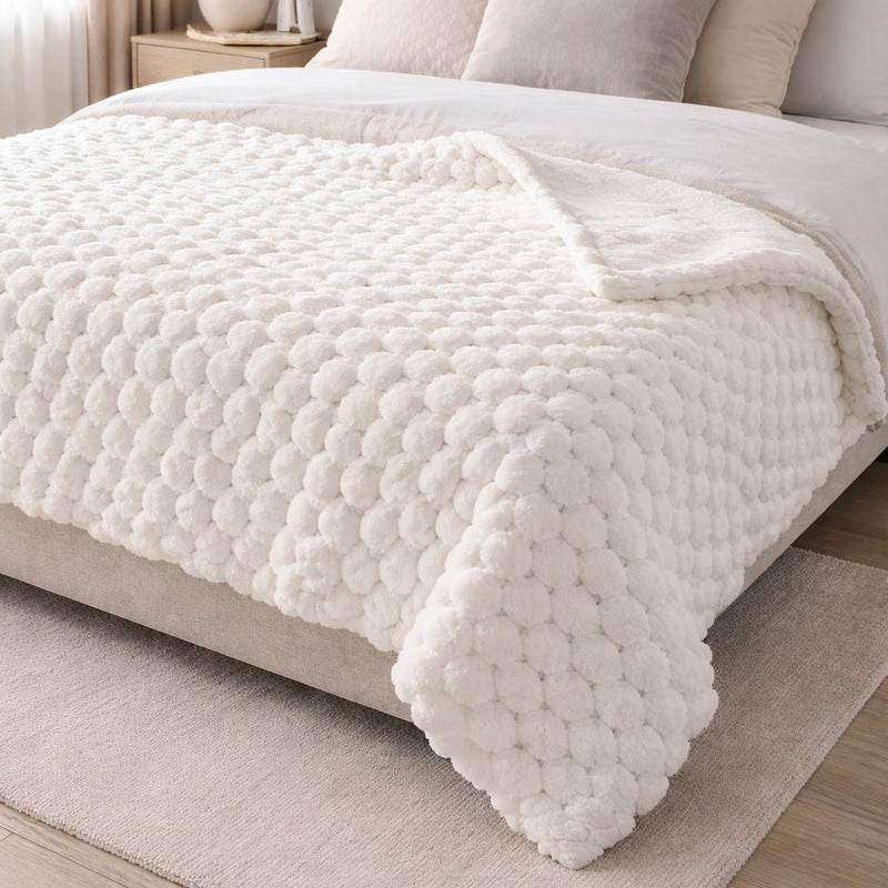Neatly made bed with white bedding and a textured white throw blanket in a bedroom setting.