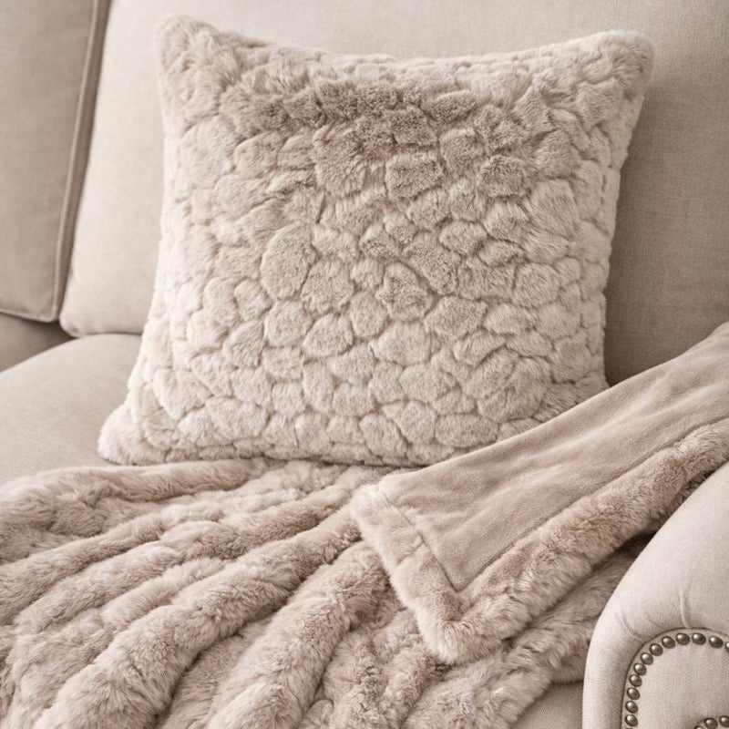 Fluffy beige pillow and throw blanket on a sofa